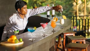 A bartender preparing drinks at a bar with various cocktails and a fruit garnish. - Reveal Courtyard in Reveal Angkor (Siem Reap)