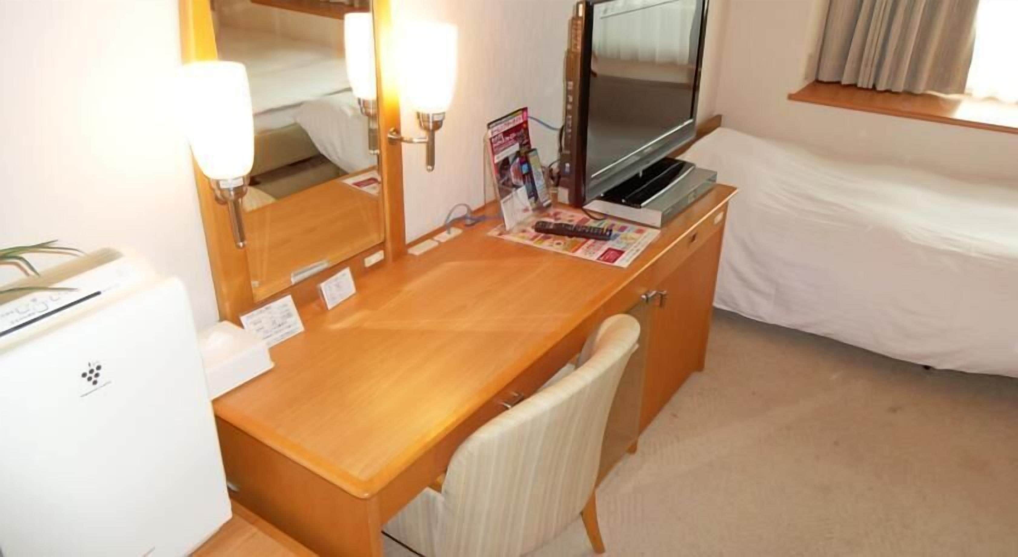 Ein Hotelzimmer mit einem Holztisch, einem Sessel, einem Fernseher und einem Bett.