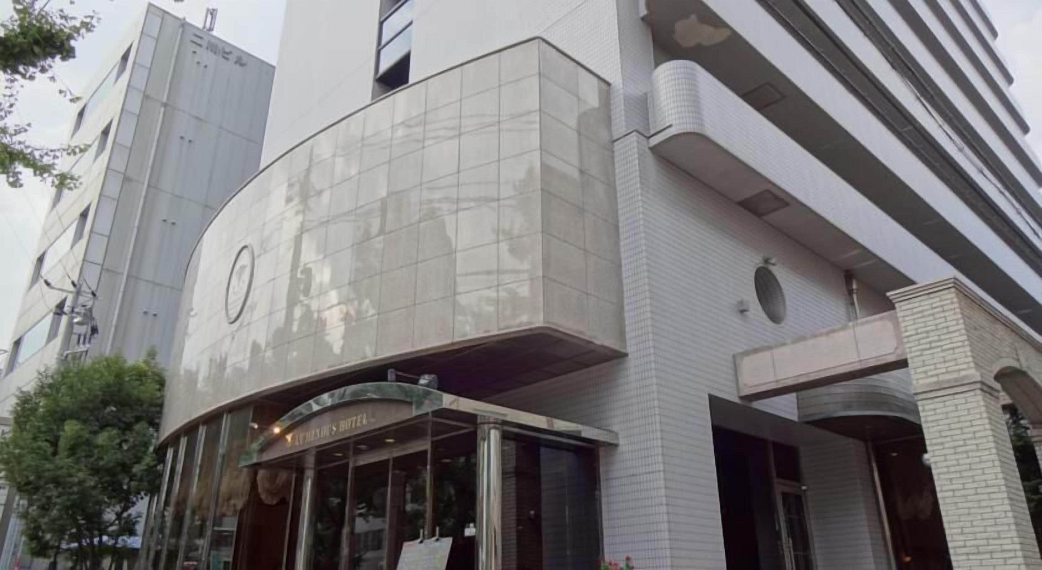 A hotel entrance with a glass facade and a sign reading "The Hexagon Hotel".