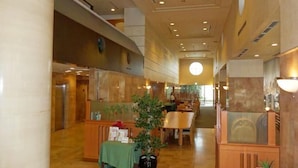 A spacious hotel lobby with a high ceiling, wooden paneling, and a central seating area with tables and chairs. -  KOBE LUMINOUS HOTEL HYOGOEKIMAE (Kobe)