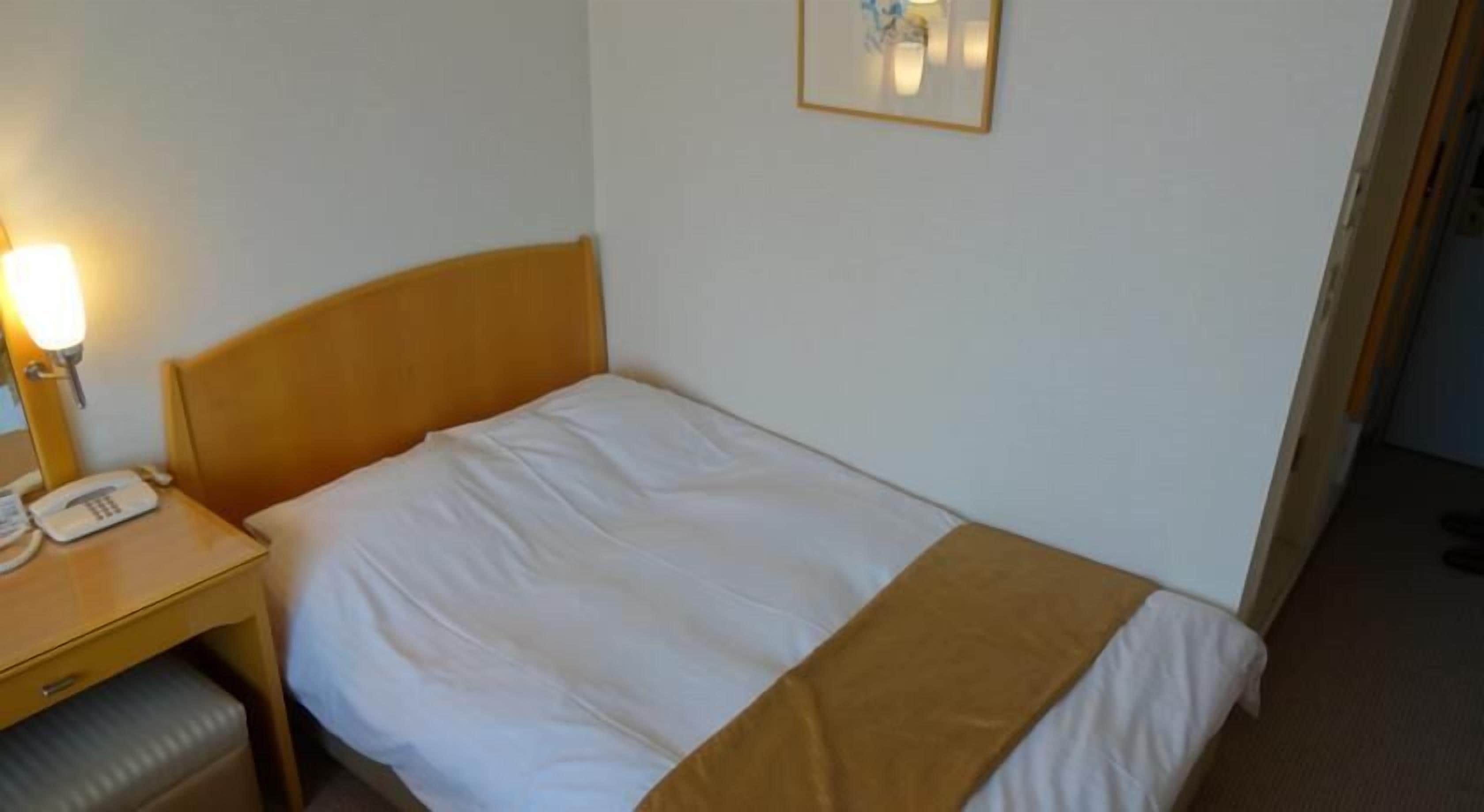 Una cama individual con cabecera de madera, una mesita de noche con lámpara y un teléfono.