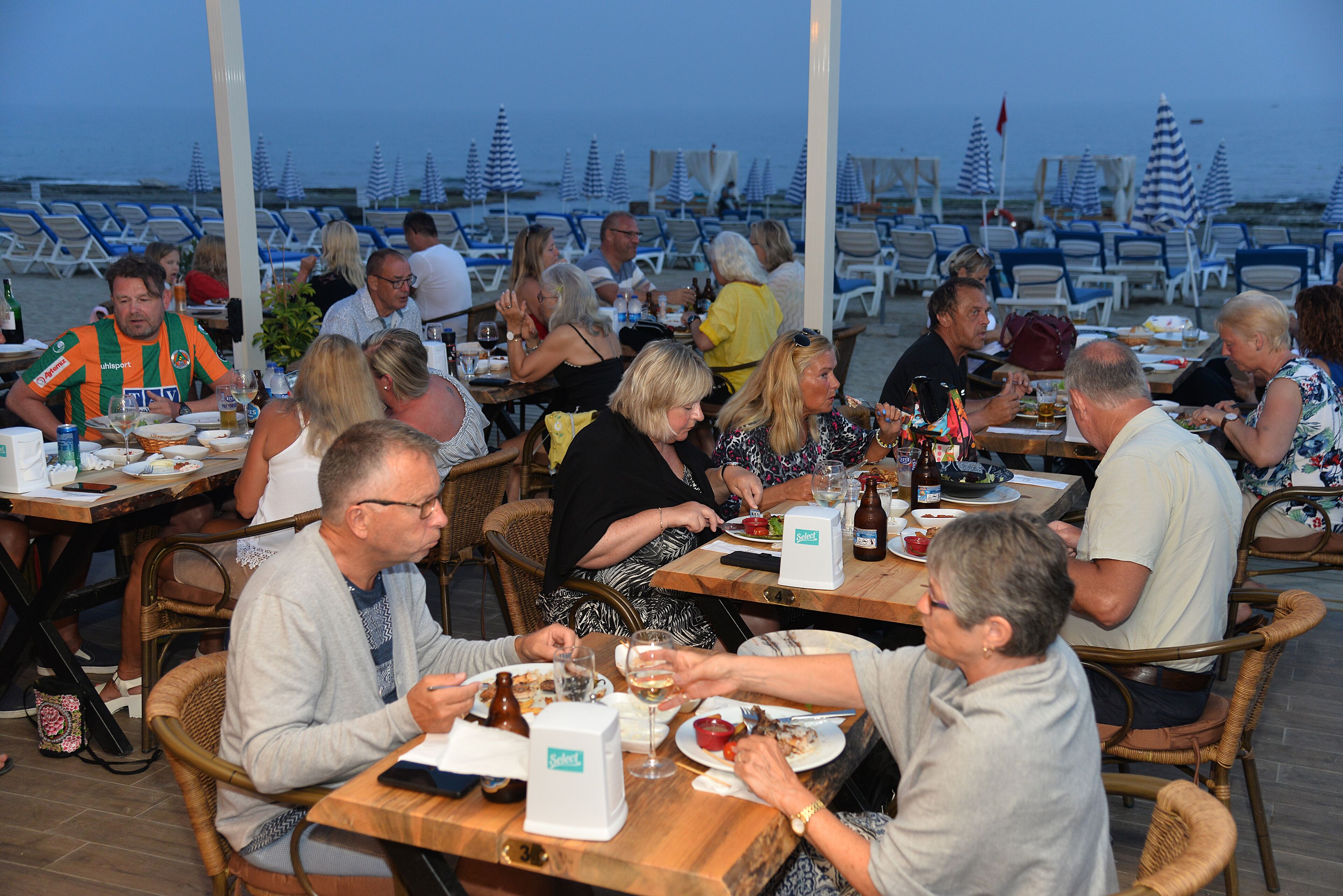 A restaurant with outdoor seating overlooking the beach, featuring wicker chairs and tables.