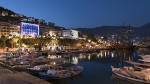 Un porto turistico al crepuscolo, con imbarcazioni ormeggiate, un hotel illuminato e montagne sullo sfondo.
