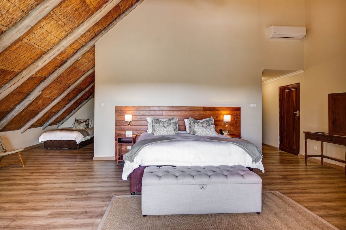 A bedroom with a sloped ceiling, a bed with a wooden headboard, a nightstand, and a bench.