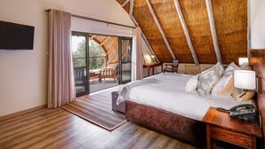 A bedroom with a large bed, wooden flooring, a ceiling fan, and a view of an outdoor deck. - Ilala Lodge Hotel (Victoria Falls)