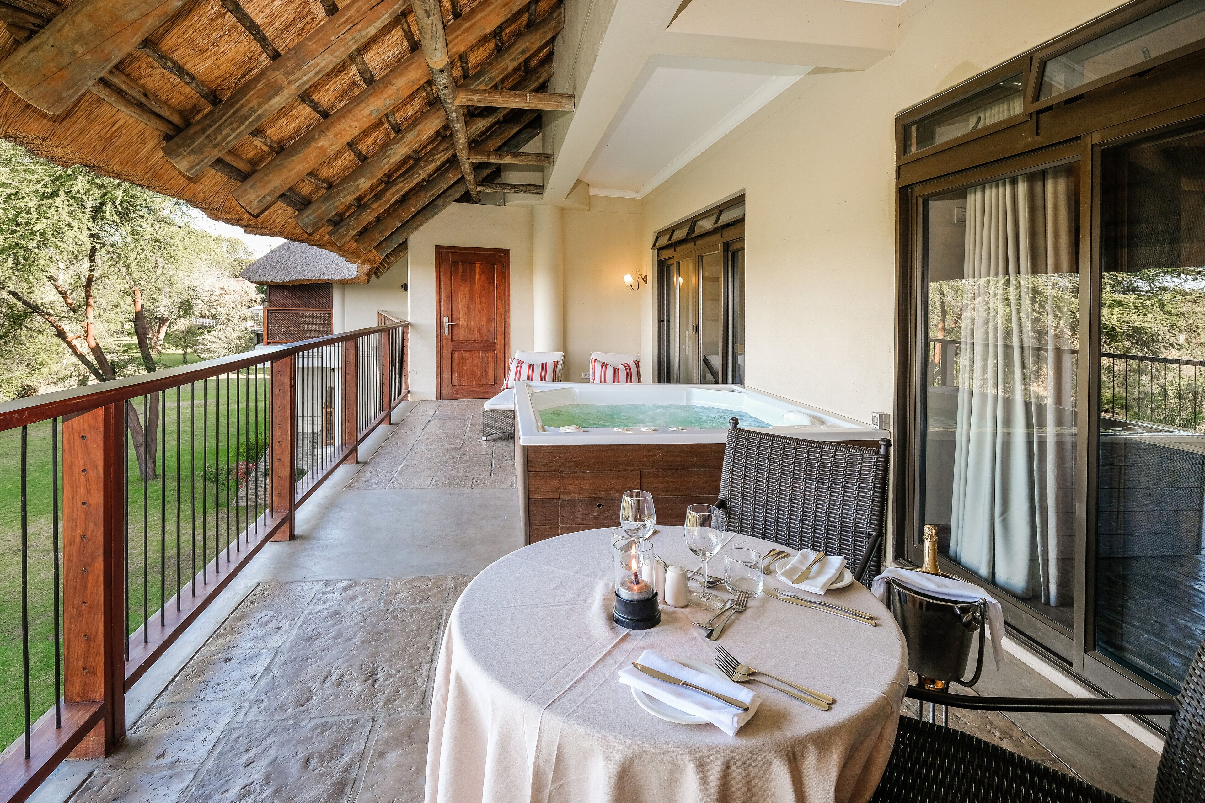 A balcony with a table set for dining, a hot tub, and a view of the outdoors.