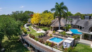 A resort with a swimming pool, outdoor seating, and a thatched-roof building. - Ilala Lodge Hotel (Victoria Falls)