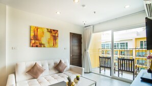 A modern living room with a white sofa, a coffee table, and a large window with a view of a yellow building. - Grand Bella Hotel (Pattaya)
