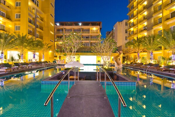 Ein Swimmingpool mit Glasbarriere und Wasserrutsche, umgeben von Palmen und Liegestühlen.