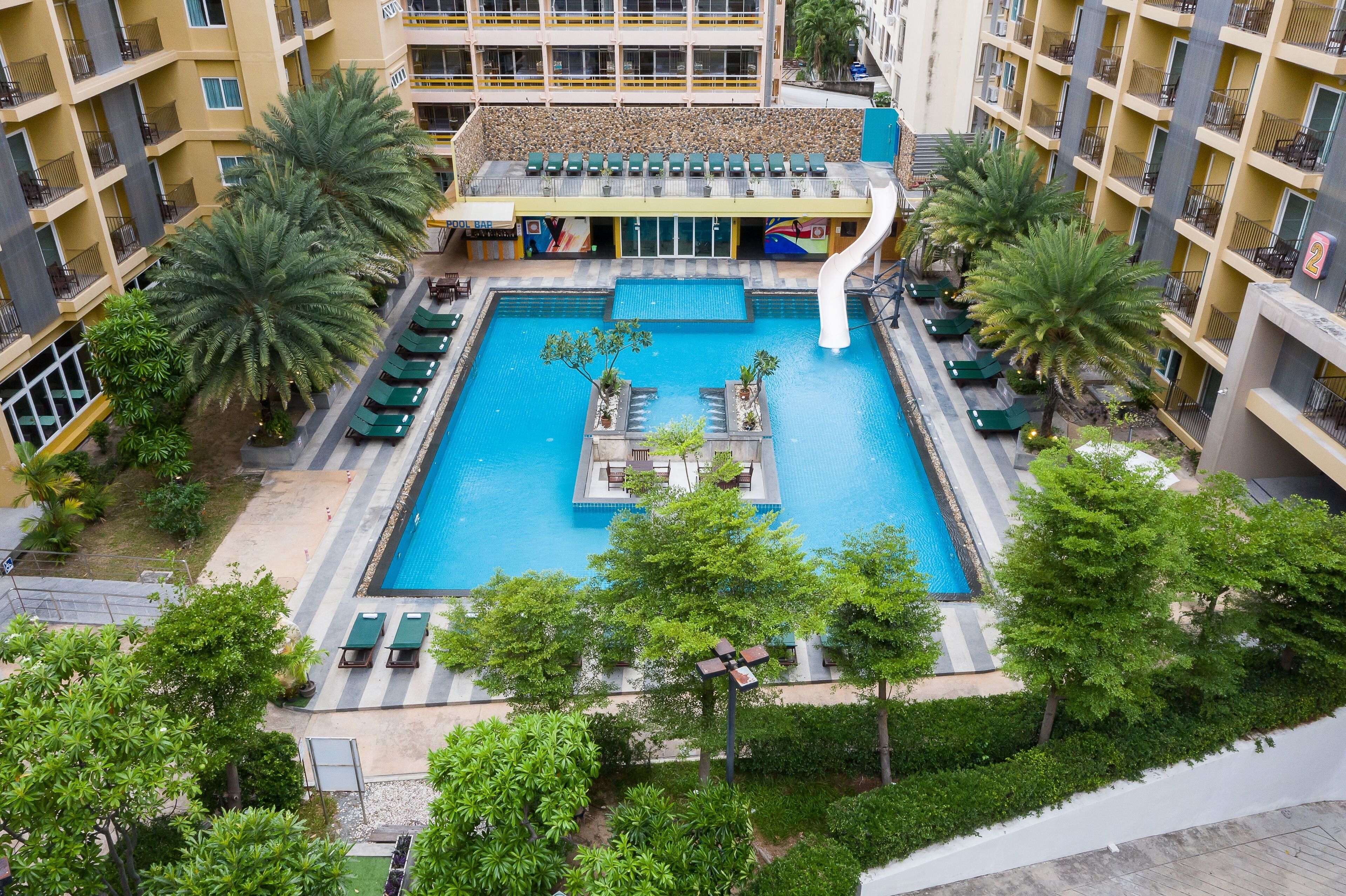 A hotel with a central swimming pool, lounge chairs, and palm trees.