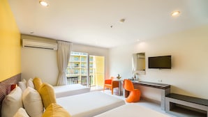 A hotel room with two beds, a desk, a chair, a TV, and a balcony with a view of buildings. - Grand Bella Hotel (Pattaya)