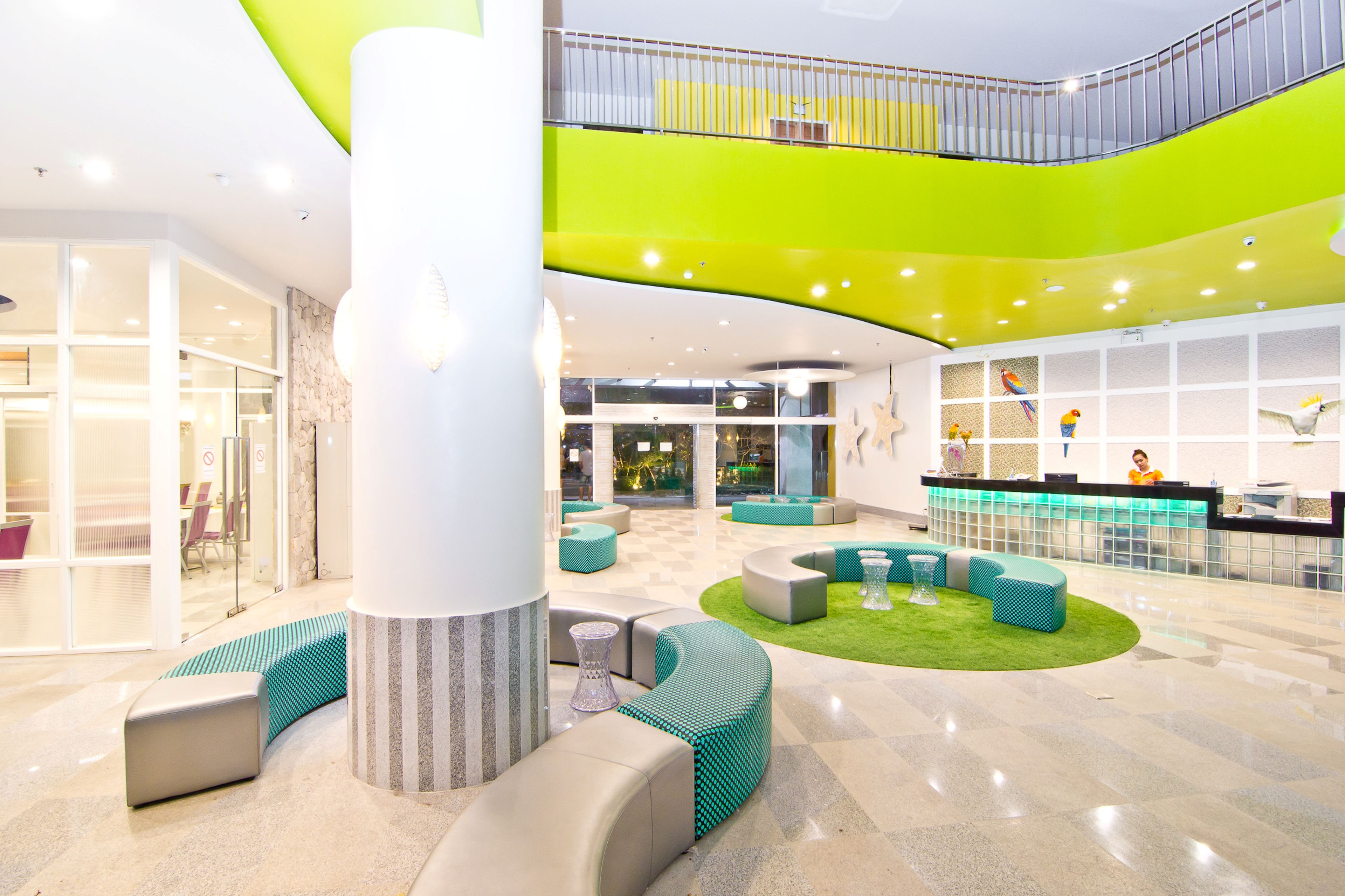 Un vestíbulo amplio con una zona de estar central, un mostrador de recepción y una escalera que conduce a un nivel superior.