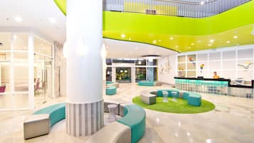 Un vestíbulo amplio con una zona de estar central, un mostrador de recepción y una escalera que conduce a un nivel superior.