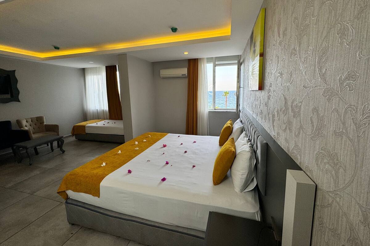 A hotel room with a large bed, a sofa, a small table, and a window with a view of the sea.