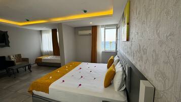 Quarto de hotel com uma cama grande, um sofá, uma mesa pequena e uma janela com vista para o mar.