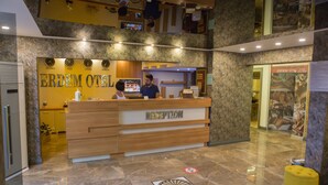 A hotel reception area with a marble floor, a reception desk, and a digital screen displaying information. - Erdem Hotel (Konyaalti)