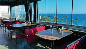 A restaurant with red chairs and tables, large windows with a view of the sea and palm trees. - Erdem Hotel (Konyaalti)