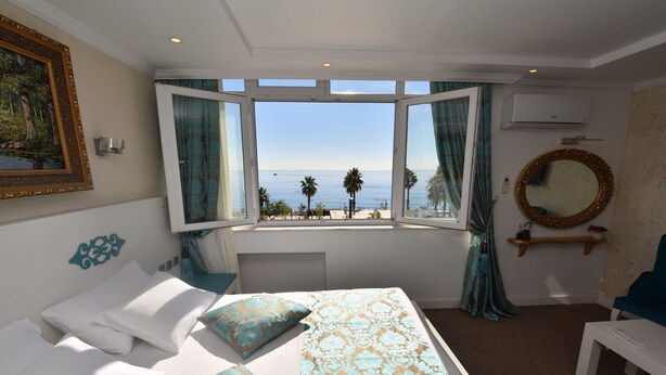 A bedroom with a large bed, a view of the sea, and a round mirror on the wall. - Erdem Hotel (Konyaalti)