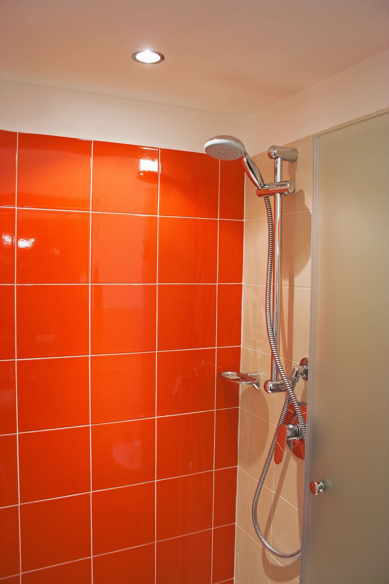 A bathroom with orange-tiled walls and a shower with a handheld showerhead and hose.