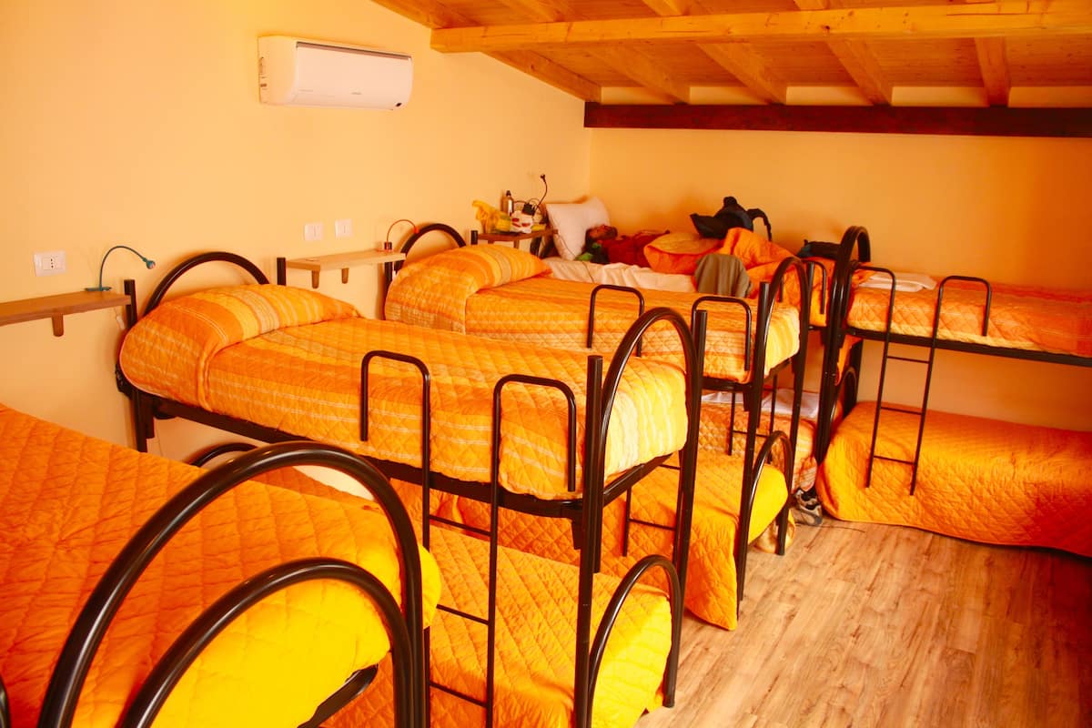 A dormitory room with bunk beds, wooden beams, and a wall-mounted air conditioner.