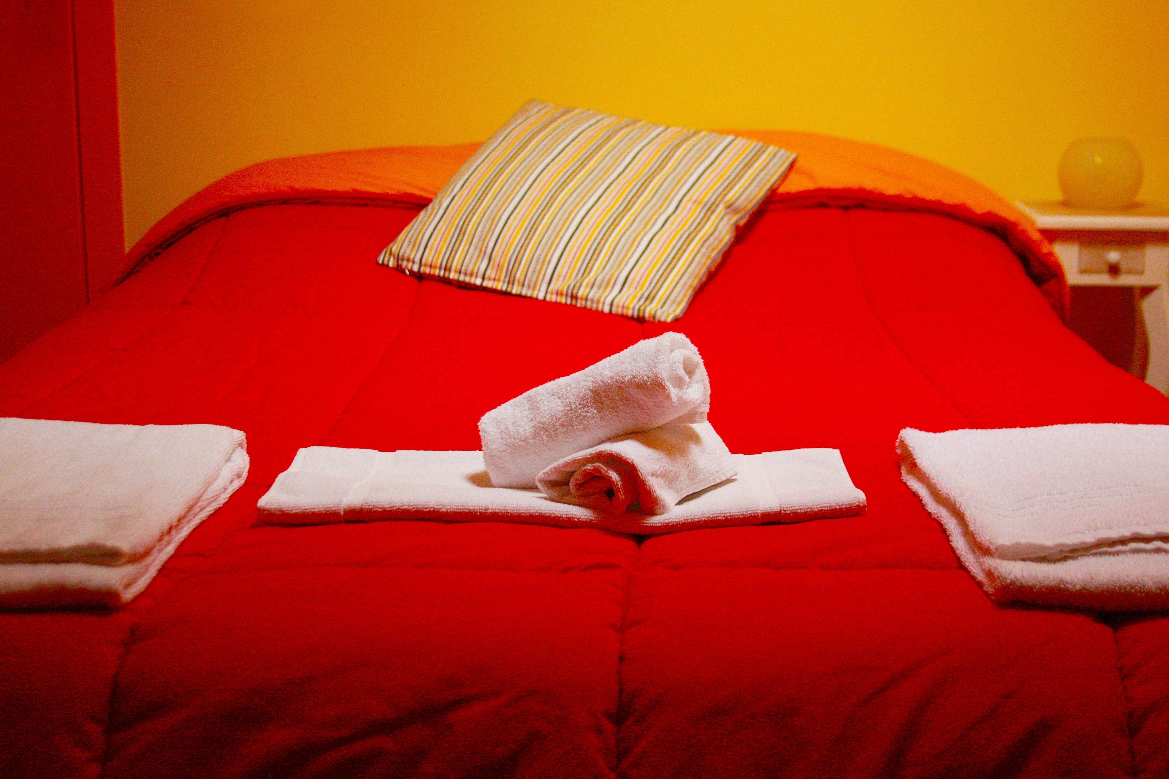 A red bed with a striped pillow and two folded towels.