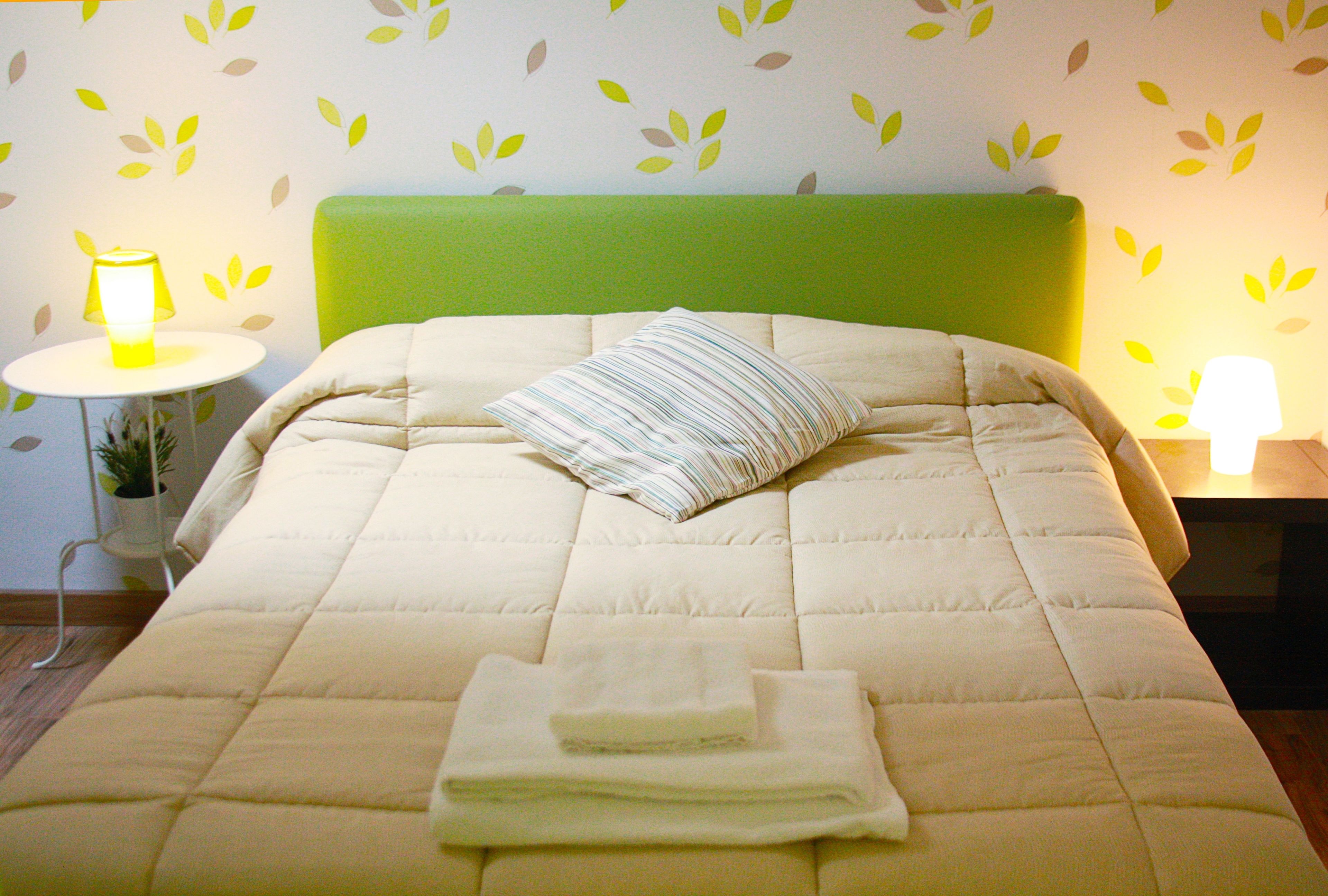 A neatly made bed with a green headboard, a striped pillow, and folded towels on the bed.