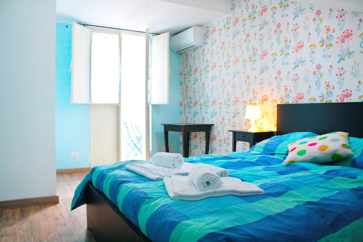 A bedroom with a bed, a nightstand, a lamp, and a window with curtains.