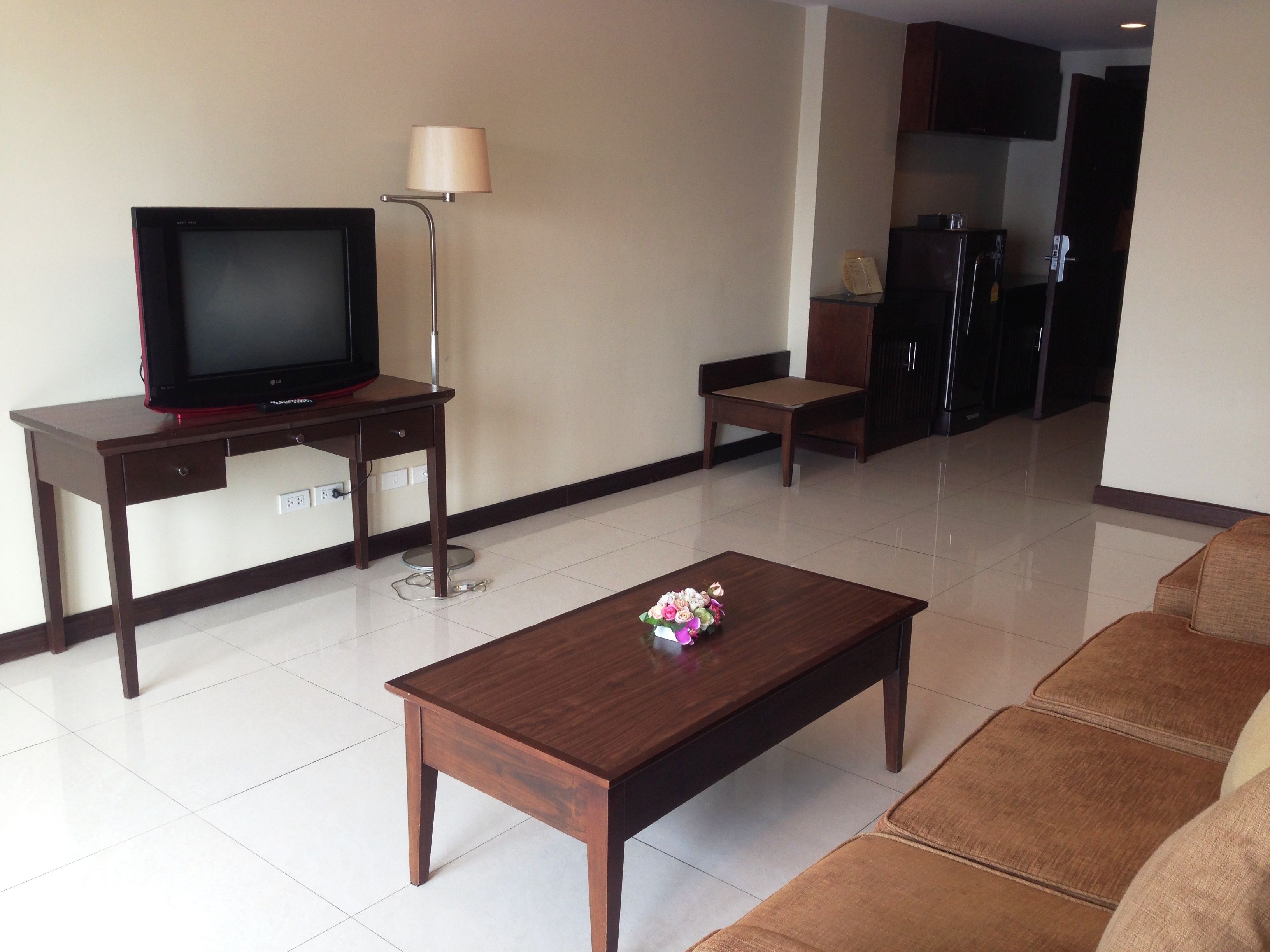 A living room with a TV on a desk, a lamp, a coffee table with flowers, and a sofa.