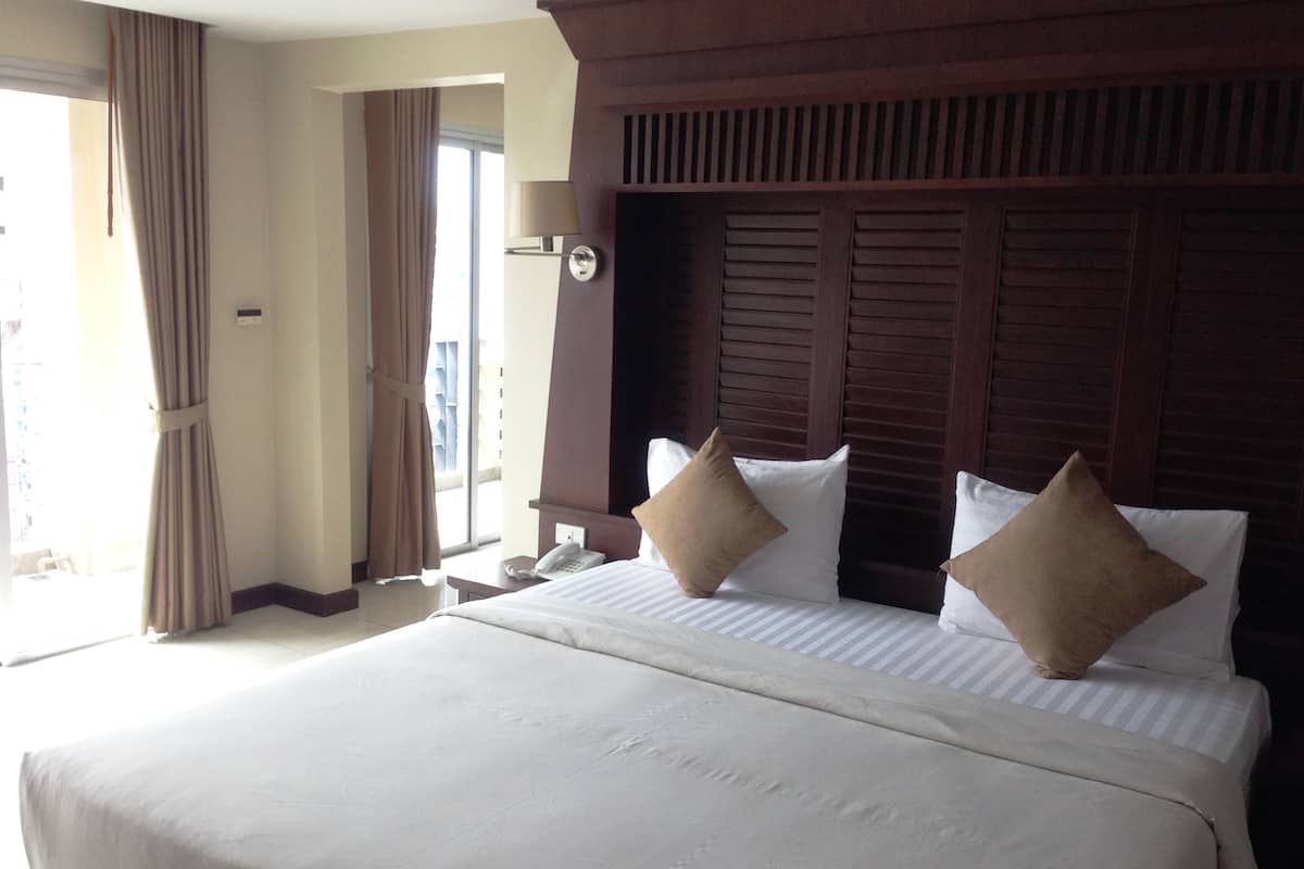 A hotel room with a large bed, two pillows, a bedside table with a lamp, and a view of the outside.