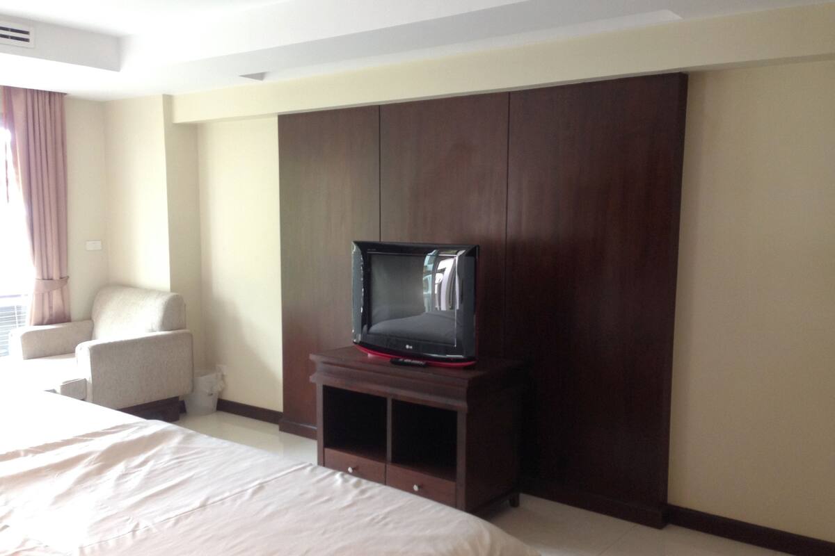 A hotel room with a bed, a TV on a wooden stand, a chair, and a wardrobe.