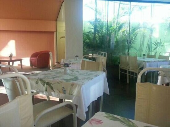 Ristorante con vista tropicale, con tavoli coperti da tovaglie bianche e sedie in vimini.
