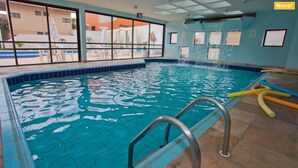 An indoor swimming pool with clear water, a tiled floor, and a view of the outside through large windows. - Ingleses Express (Florianopolis)