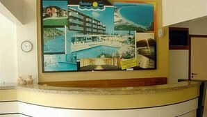A reception desk with a large poster of a resort, a clock, and a door to the right. - Ingleses Express (Florianopolis)
