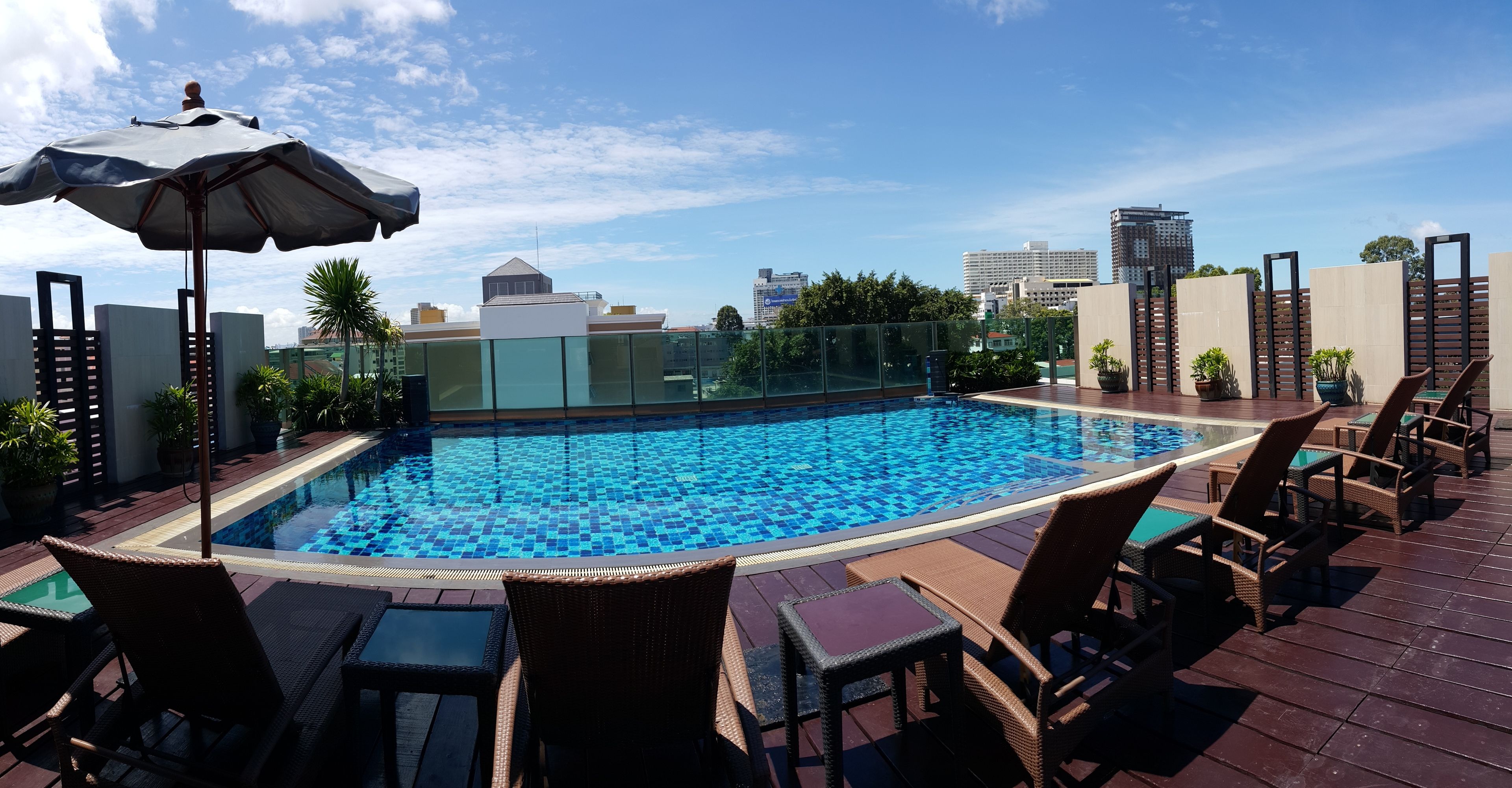 A rooftop pool with clear blue tiles, surrounded by wicker lounge chairs and a large umbrella.