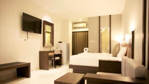 A modern hotel room with a large bed, a desk, a chair, a flat-screen TV mounted on the wall, and a sofa.