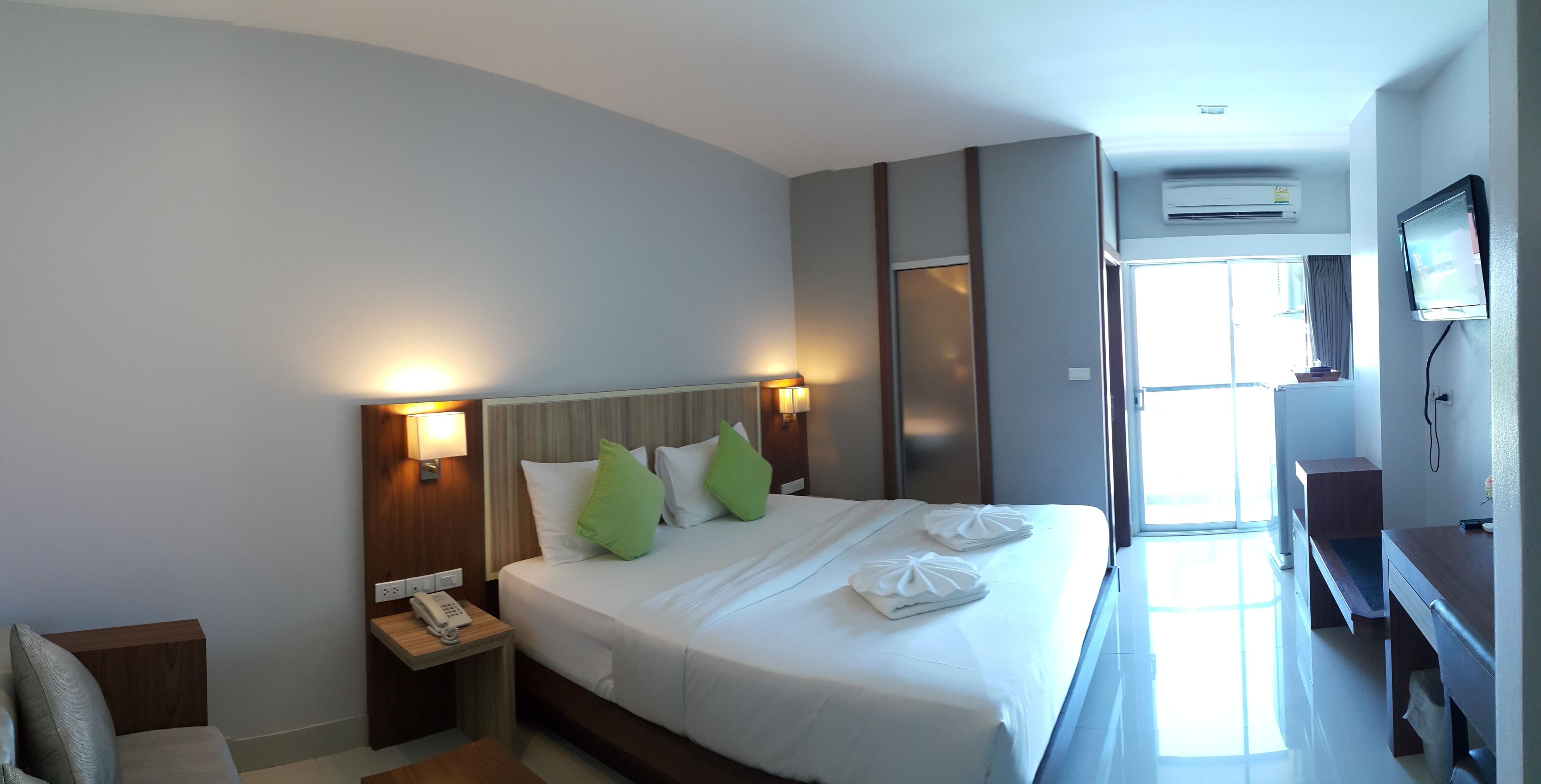 A hotel room with a bed, nightstand, and a desk with a chair.