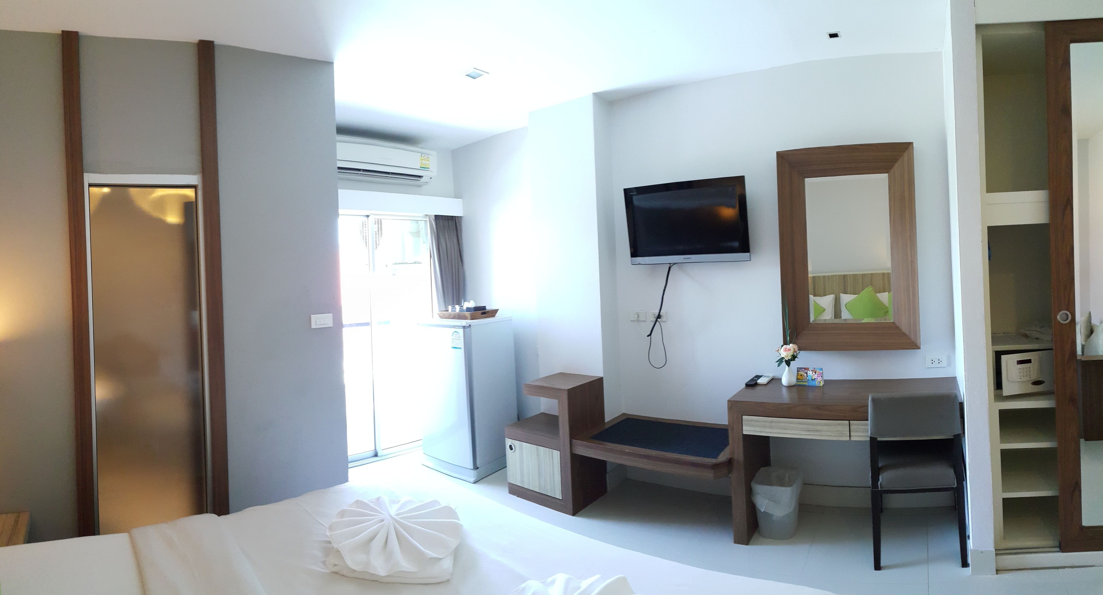 A hotel room with a bed, a desk, a chair, a TV, a mirror, and a wardrobe.