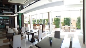 A spacious indoor area with multiple seating arrangements, including tables and chairs, and a bar area with shelves of bottles.