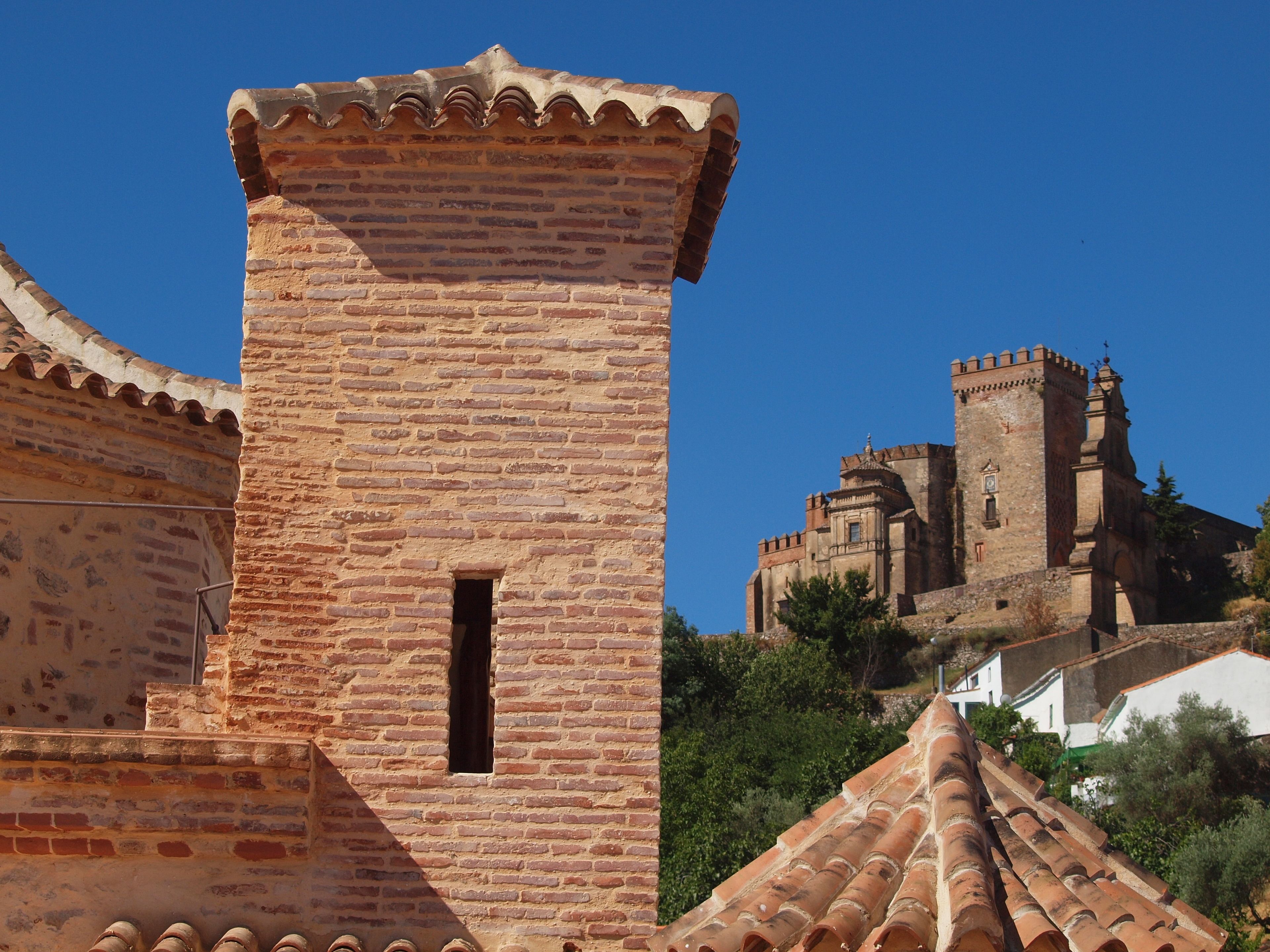 Una torre de ladrillo histórico con una pequeña ventana, parte de una estructura fortificada más grande con almenas.
