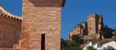 Una torre de ladrillo histórico con una pequeña ventana, parte de una estructura fortificada más grande con almenas.