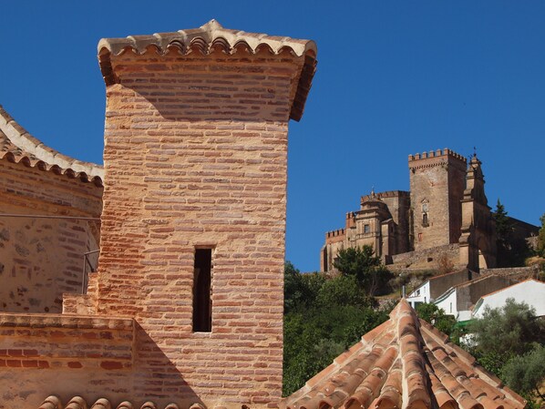 Una torre de ladrillo histórico con una pequeña ventana, parte de una estructura fortificada más grande con almenas.