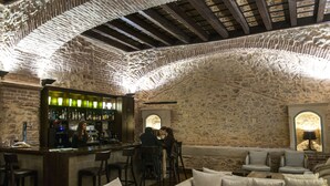 A bar area with stone walls, wooden beams, and a bar counter with stools. There are cushioned seating areas and a lamp in the corner. - Hotel Convento Aracena & Spa (Aracena)