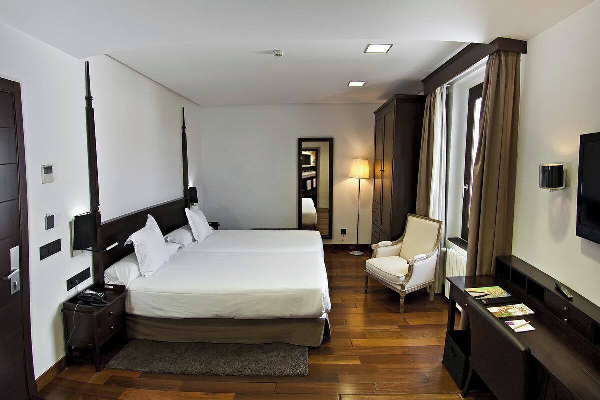A hotel room with a large bed, bedside tables, a chair, a desk, a TV, and a lamp.