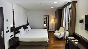 Una habitación de hotel con una cama grande, mesitas de noche, una silla, un escritorio, un televisor y una lámpara.