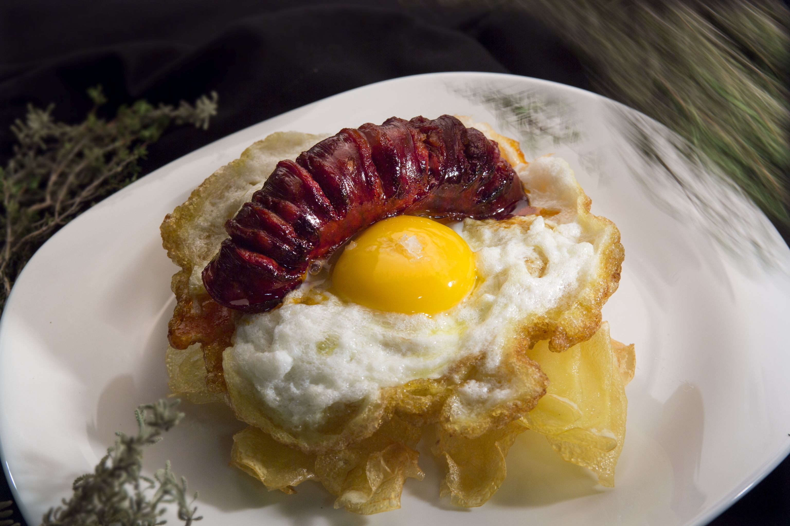 A plate with a fried egg, bacon, and a piece of fried potato.
