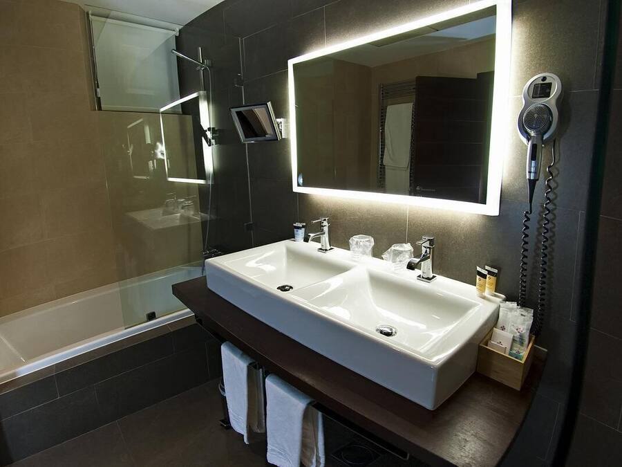 A modern bathroom with a dual sink vanity, a large mirror, and a hairdryer mounted on the wall.