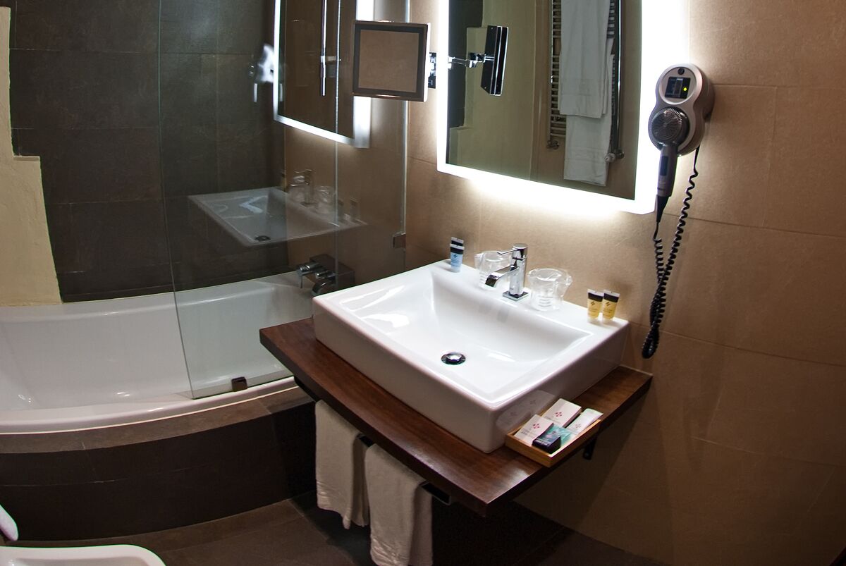 Un bagno con lavandino bianco, uno specchio, un asciugacapelli e un portasciugamani.