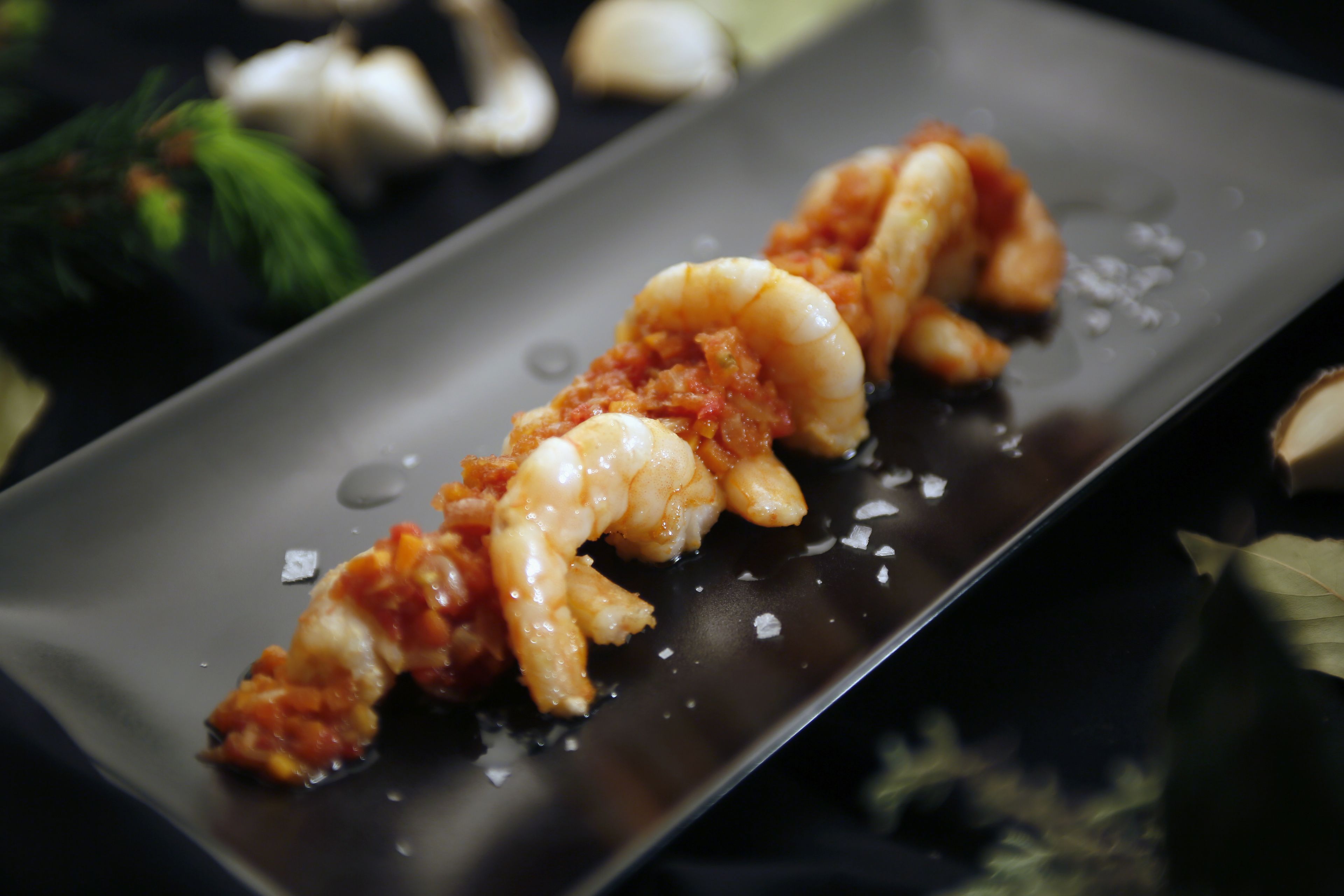 A rectangular plate with a seafood dish, possibly shrimp, on a dark background with some scattered salt crystals.