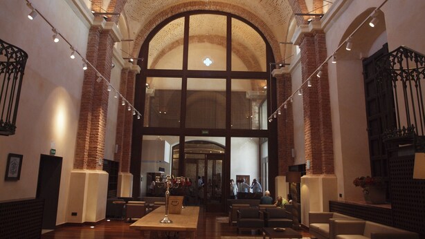 A spacious lobby with high ceilings, exposed brick walls, and a large arched window. - Hotel Convento Aracena & Spa (Aracena)