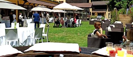 An outdoor dining area with tables and chairs, umbrellas, and people dining.